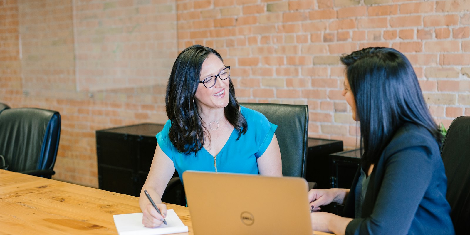 Two business professionals in consultation — one taking notes, one listening